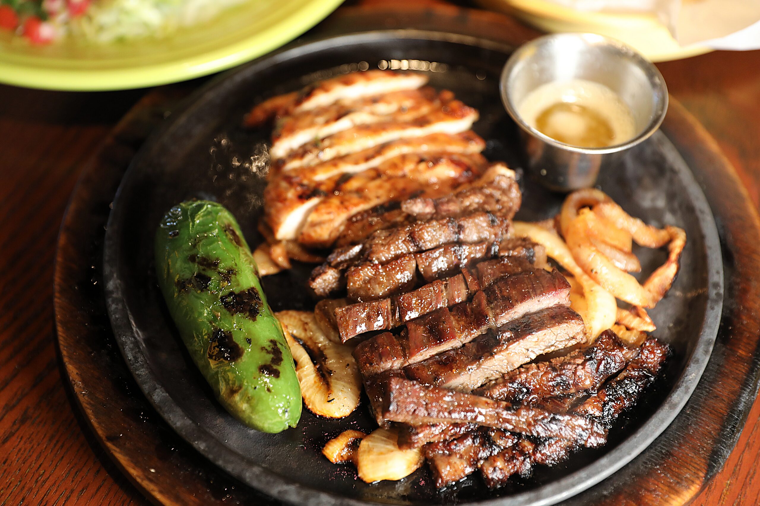 Beef and chicken fajitas arrive sizzling with grilled onions and a whole roasted jalapeño at Cadillac Bar. | Photo by Cadillac Bar