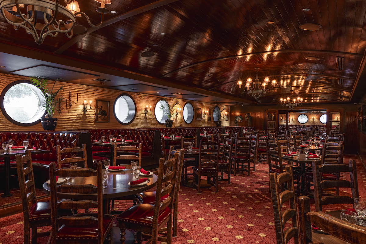 El Molino - DiningOut Cozy upscale dining room with wood-paneled ceiling, round porthole windows, red leather booths, and wooden chairs.