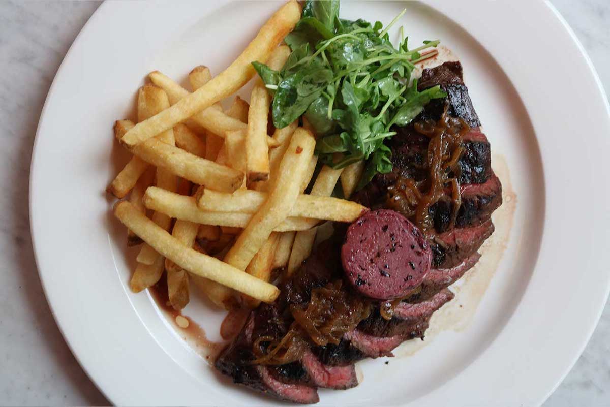 Bistro Niko serves its classic steak frites with a generous pile of golden fries and greens. | Photo by Bistro Niko