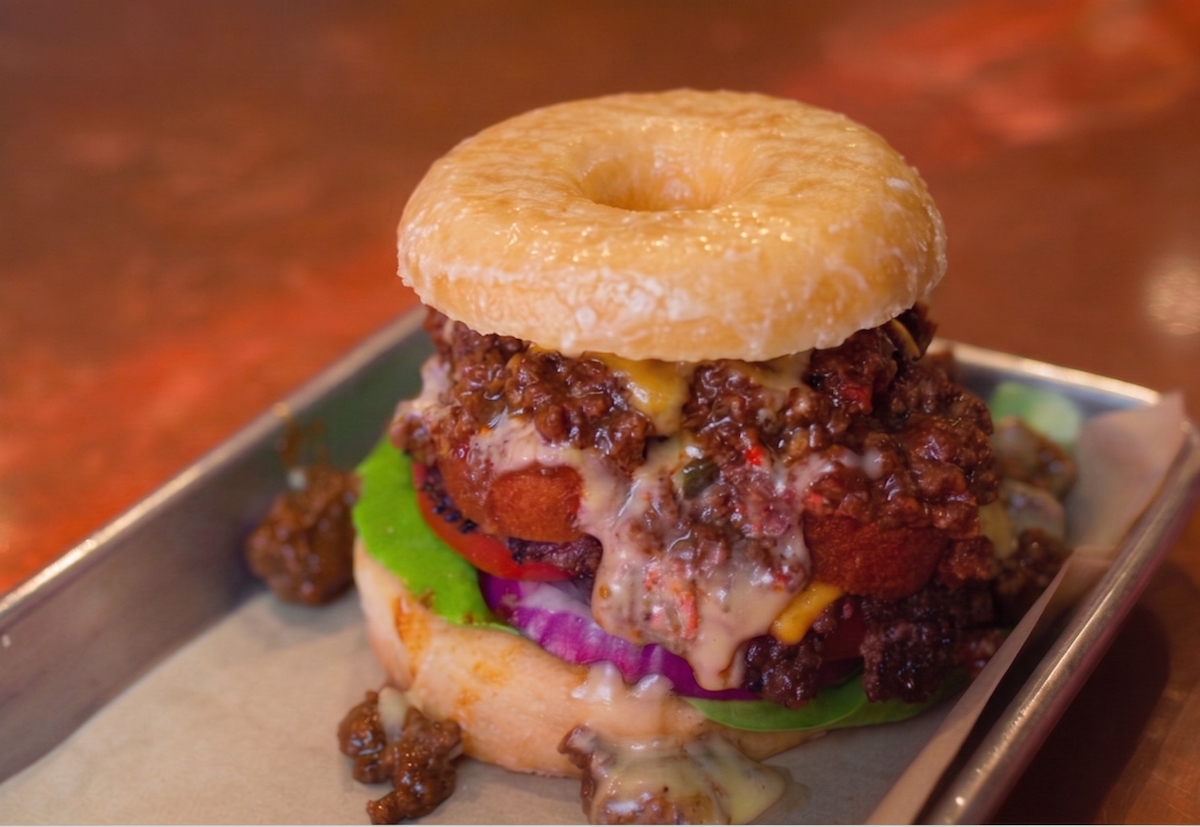 Burger Schmurger DAL - DiningOut Burger Schmurger goes big for State Fair season with the Big Tex, stacking a double smashburger with a corn dog, Texas chili, queso, and all the fixings between a glazed doughnut. | Photo by Burger Schmurger