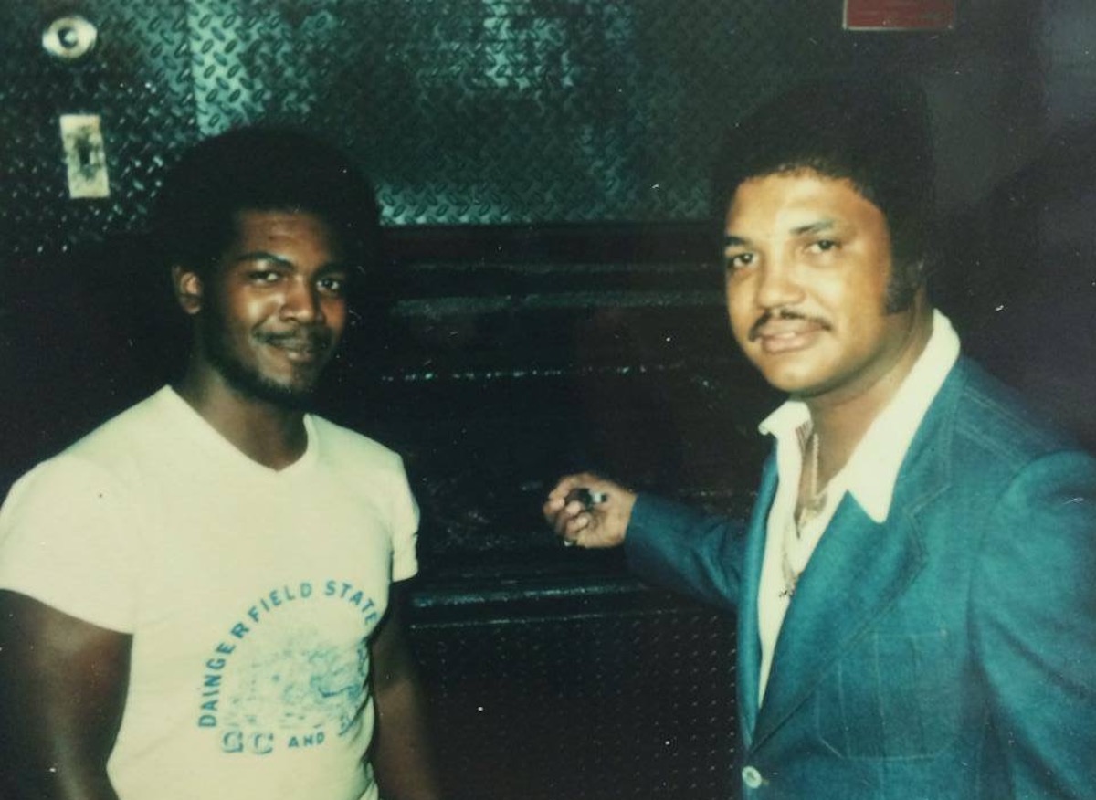 Smokey John’s founder “Smokey” John Reaves, right, and his cousin Douglas “Rent” Spaglin, one of the original members of the family-run restaurant team, pose in front of their first pit. | Photo by Smokey John's BBQ