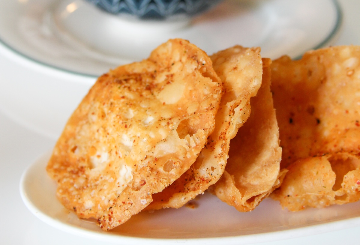 Golden, seasoned crackers or biscuits stacked on a white spooned dish, close-up detail shows crispy texture and specks of seasoning