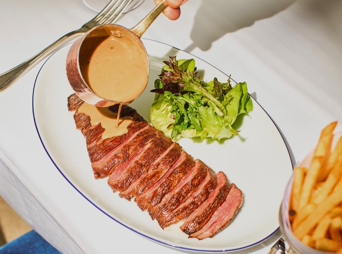 Le Bilboquet’s steak frites delivers classic French bistro appeal with hanger steak, peppercorn sauce, greens, and fries. | Photo by Le Bilboquet