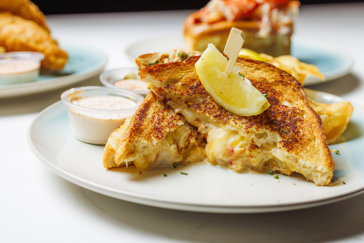 A customer favorite, Dock Local's decadent lobster grilled cheese combines generous chunks of lobster and shrimp with homemade queso, Swiss, Gouda, and a touch of sriracha, served with lobster bisque for dipping. | Photo by Samantha Marie Photography