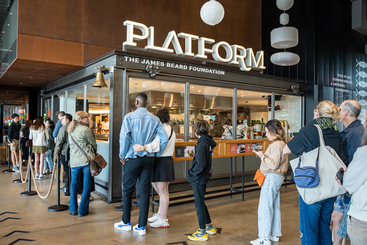 Line of diverse customers waiting to order at a cafe counter labeled Platform, The James Beard Foundation, in a modern interior.