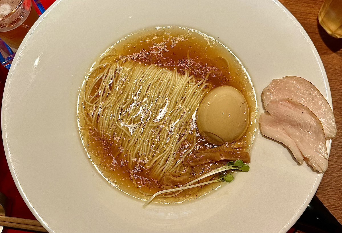 Bowl of ramen with broth, thin noodles, soft-boiled egg, bean sprouts, and sliced chicken on the rim.