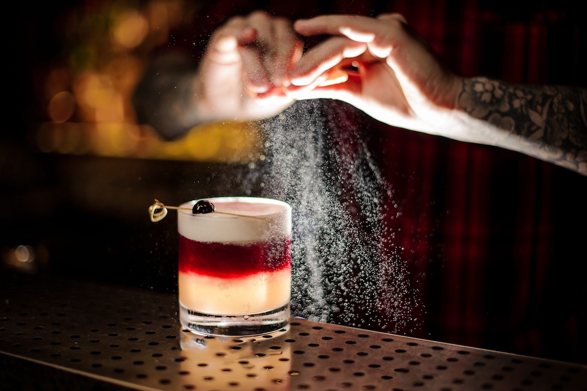 Mixologist sprinkling orange juice into a glass of sweet flaky cocktail denver cocktails