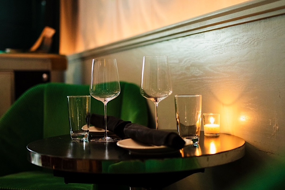 Romantic restaurant table set with two wine glasses, a water glass, napkin, and a lit candle in warm light.