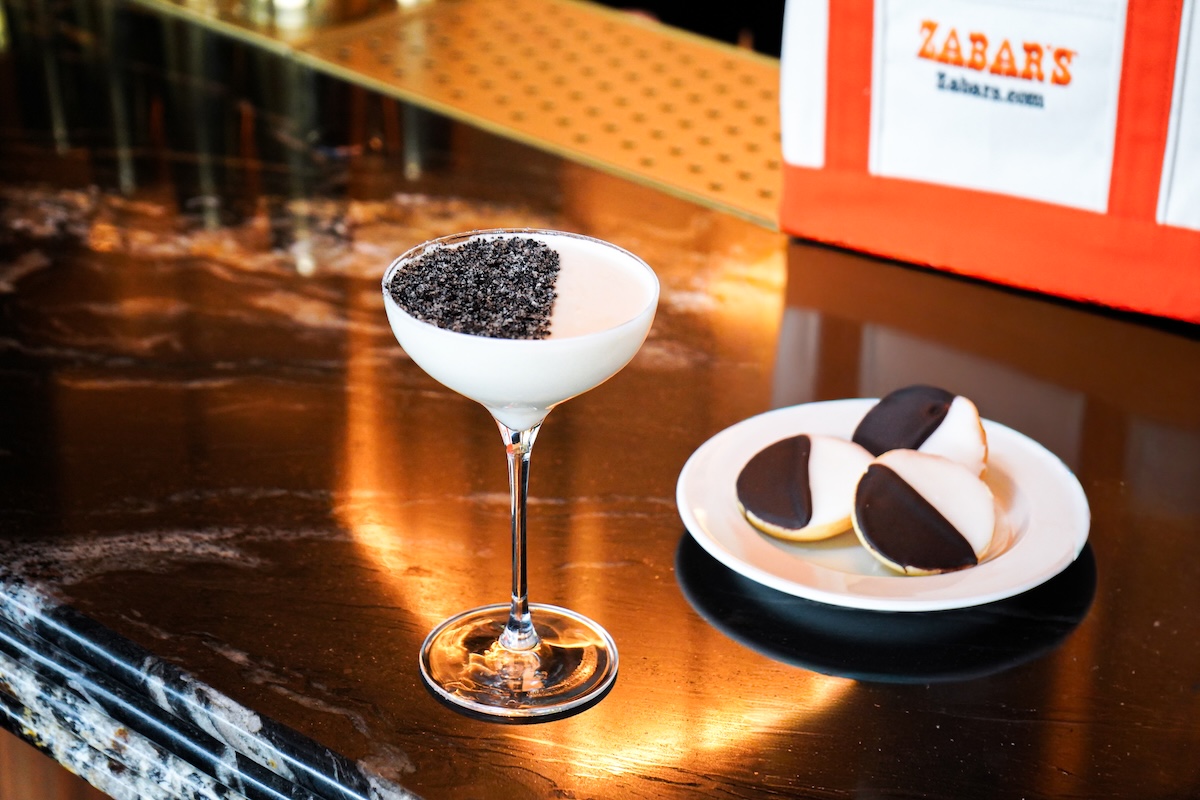 NY_TheView_BlackAndWhite_CreditKristenHubby - DiningOut Cocktail in a coupe glass with Oreo crumble rim on a polished bar, beside a plate of chocolate-dipped cookies.