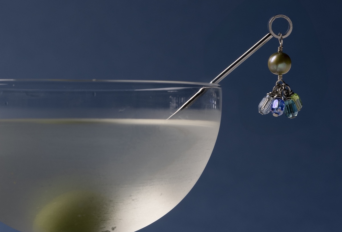 Close-up of a cocktail glass with a metal pick holding a pearl bead and dangling crystal charms.